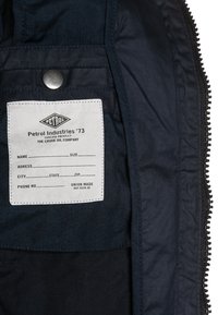 White fabric label reading "Petrol Industries '73," with blank fields for name, size, address, city, state, zip, and phone number sewn inside a dark jacket.