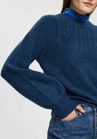 Blauer Strickpullover mit strukturiertem Muster, gerippten Bündchen und hohem Kragen, mit dezenten helleren Farbsprenkel durchgehend.
