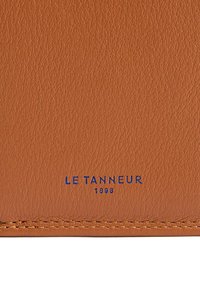 Prodotto in pelle color nocciola con finitura testurizzata, caratterizzato da testo in rilievo blu "LE TANNEUR 1898" e cuciture a contrasto lungo il bordo.