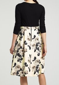 Top nero a costine con maniche lunghe abbinato a una gonna floreale crema con rose nere e beige e una finitura texture.