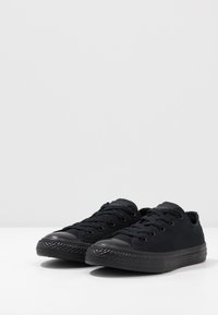 Sneaker neri in tela con punte in gomma, suole testurizzate, sei asole e un design di lacci piatti. Superficie liscia con un'estetica minimalista.