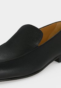 Chaussure de ville noire en cuir à enfiler, talon bas et bout arrondi lisse, avec une finition texturée et une doublure intérieure couleur fauve.