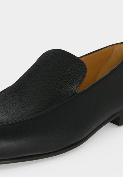 Chaussure de ville noire en cuir à enfiler, talon bas et bout arrondi lisse, avec une finition texturée et une doublure intérieure couleur fauve.