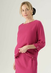 Top fucsia con scollo a barca, maniche a tre quarti e polsini ripiegati. Tessuto morbido con una finitura liscia e dettagli in oro.