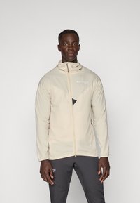 Light beige jacket with a high collar, full zip, and zippered pockets. Features a textured upper and triangular accent on the chest.