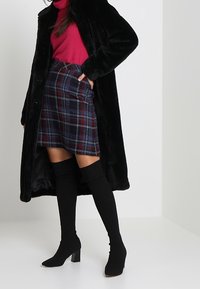 Mustat keinokuituiset turkistakit, punainen poolopaita, sininen, punainen ja valkoinen ruudullinen minihame, yhdistettynä mustiin polven ylle ulottuviin korkokenkiin.