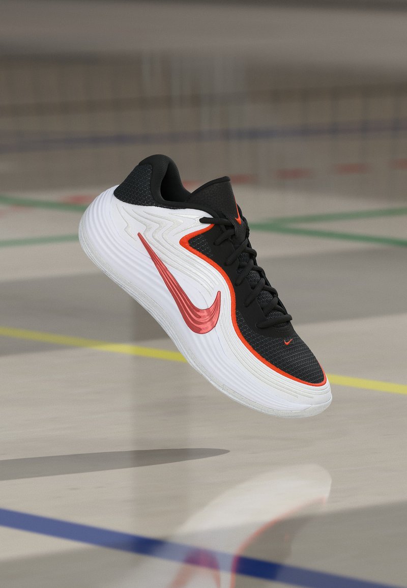 Fekete-fehér sportcipő piros kiemelésekkel és pipa logóval, egy konditerem padlója felett lebeg, amelyen pályajelölések láthatók.