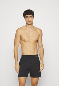 Shorts noirs en coton avec taille élastique et une seule fermeture à bouton à l'avant. Texture lisse avec un design simple.