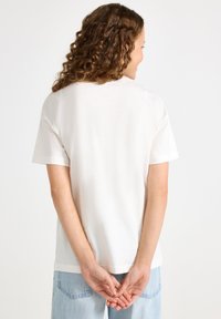 Hvid bomulds t-shirt med korte ærmer, afslappet pasform og en glat tekstur. Bagfra ses et enkelt design og standard rund hals.