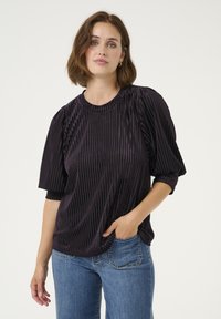 Blusa negra plisada con escote redondeado y mangas abullonadas, combinada con jeans azules. La tela tiene un brillo sutil y una textura.