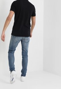 Černé polo tričko spárované s světle modrými džíny a bílými teniskami, s slim fit střihem a krátkým rukávem.