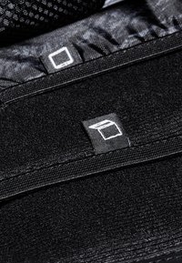 Tissu noir avec une surface texturée et des accents de couture. Présente une petite étiquette de logo carrée en blanc sur le matériau noir.