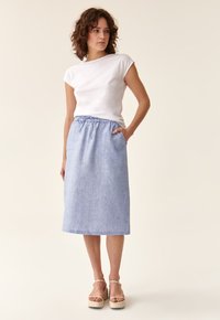 Gonna di lino azzurro chiaro con vita elasticizzata e tasche, abbinata a una t-shirt bianca aderente e sandali beige con plateau.