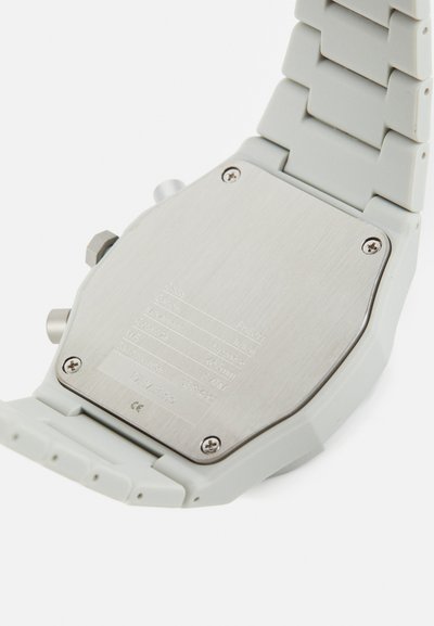 Γκρίζο ρολόι με σιλικονέινα λουράκι και πίσω μέρος από βουρτσισμένο ανοξείδωτο χάλυβα που εμφανίζει επισημάνσεις και προδιαγραφές. Διαθέτει κομψό, γωνιακό σχέδιο.