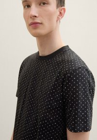 Black short-sleeve T-shirt featuring a subtle geometric pattern in silver. Made from soft cotton with a round neckline and relaxed fit.