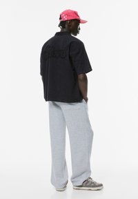 Cămașă neagră cu mânecă scurtă, cu broderie "Stand" pe spate, pantaloni de trening gri și o șapcă roz cu accente stelare și o curea.