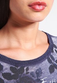 Sininen kukkateemainen paita, jossa on ribbausmainen kaula-aukko. Pehmeä kangas, jossa on rento istuvuus, tummia lehtiä vaalealla taustalla.