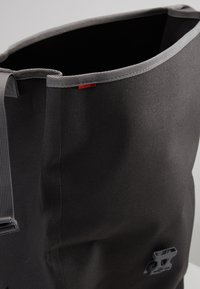 Borsa a spalla in tessuto nero con bordo superiore grigio. Presenta manici resistenti e un piccolo logo grigio sul lato. Materiale testurizzato per una presa migliore.