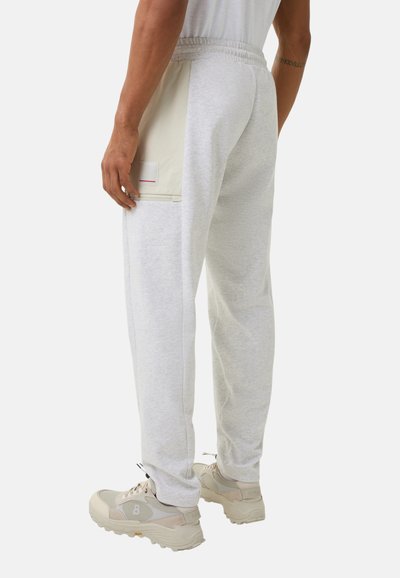 Graue Sweatpants mit elastischem Bund, Seitentasche und einem beigen Stoffeinsatz. Strukturierter Baumwollmix, taillierte Passform. Kombiniert mit hellen Turnschuhen.
