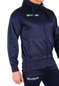 Dunkelblaue Trainingsjacke aus glattem Stoff. Mit einem Reißverschluss vorne, Kapuze und weißem GIVOVA-Logo. Enthält Seitentaschen und gerippte Bündchen.