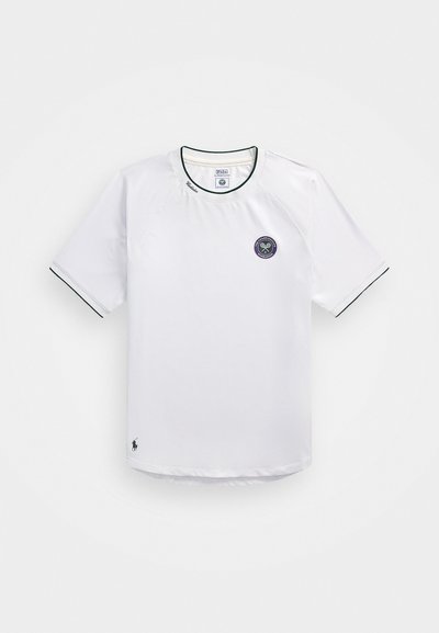 Vit kortärmad tennisskorta med rundad halsringning, grön trim, en cirkulär lila logotyp och varumärke på kragen och nederkanten.