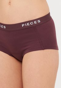 Maroonske bešavne djevojačke gaćice s širokim elastičnim pojasom na kojem je označeno "PIECES" u bijeloj boji. Imaju glatku teksturu i prilagođeni dizajn.