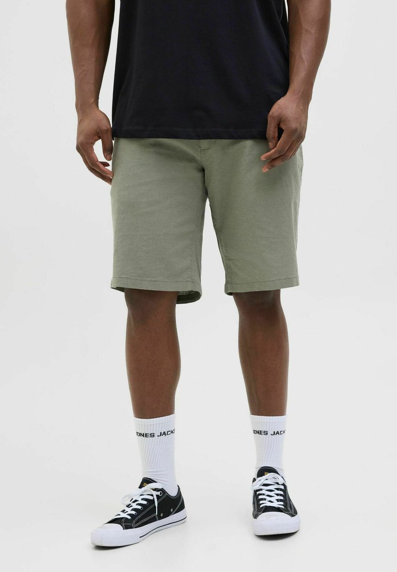Shorts kaki à coupe droite, en coton, avec un ourlet roulé, associés à des baskets noires et des chaussettes blanches. Design simple et style décontracté.