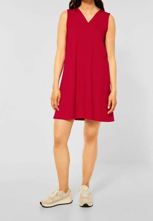 Rotes ärmelloses Kleid mit V-Ausschnitt und A-Linie-Silhouette, aus glattem Stoff gefertigt, kombiniert mit neutralen sportlichen Sneakern.
