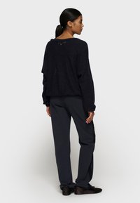 Zwarte gebreide trui met een losse pasvorm, verlaagde schouders en een open rugdetail. Gecombineerd met donkergrijze slim-fit broek en bruine schoenen.