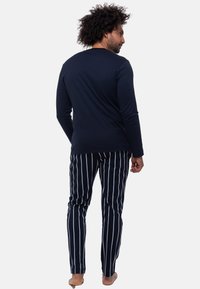 Marineblaue Langarmshirt, kombiniert mit schwarz-weißen gestreiften Schlafanzughosen, die ein figurbetontes Design und eine weiche Textur aufweisen. Rückansicht gezeigt.