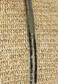 Wpleciona torba słomiana o teksturowanej beżowej powierzchni z pionowym paskiem ciemnych cekinów, co dodaje kontrastu i detali do projektu.