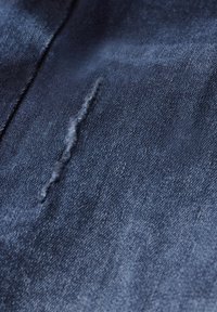Denim stof in donkerblauw met een gladde textuur, met een opvallende rafelige naad en subtiele variaties in schaduw.