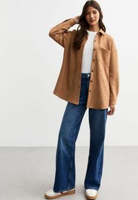 Bruine suède button-up shirt met een enkele borstzak, gecombineerd met brede spijkerbroeken in blauwe denim en witte sneakers. Glad textuur, losse pasvorm.