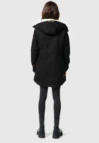 Zwarte parka met een met bont gevoerde capuchon, lange mouwen en een gebogen zoom, gecombineerd met donkere jeans en zwarte enkellaarzen.