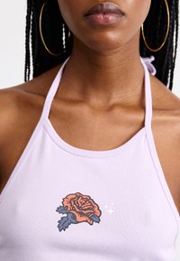 Top halter lilac realizzato in tessuto a coste, caratterizzato da una grafica di una dettagliata rosa rossa con foglie blu sul lato sinistro.