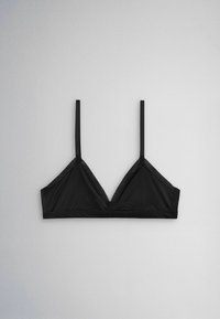 Čierny trojuholníkový bralette s tenkými nastaviteľnými ramienkami položený na svetlo šedom pozadí.