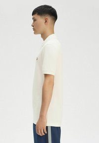 Polo shirt bianco in cotone con maniche corte, colletto a contrasto e logo ricamato sul petto. Orlo dritto. Il modello indossa pantaloni blu navy.