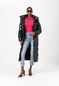Črn sijajni dolgi puffer plašč s kapuco, složen preko prilegajoče roze majice in skrajšanih modrih jeans hlač, zaključen s črnimi visokimi petami.