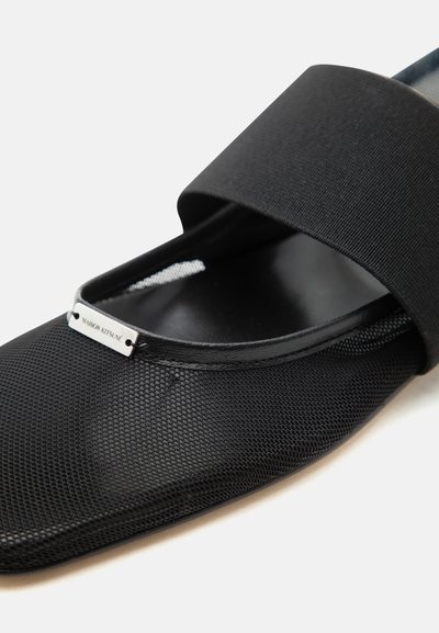 Μαύρο παπούτσι με πλέγμα, χωρίς κορδόνια, με φαρδιά ελαστική λωρίδα και μικρή μεταλλική ετικέτα με την επιγραφή "Maison Kitsuné" κοντά στην περιοχή των δακτύλων.