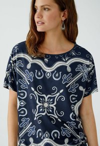 Haut bleu marine en tissu lisse, orné de motifs blancs et bleus complexes, à manches courtes et à col rond.