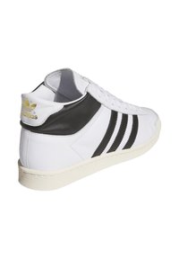 Sneakers bianchi in pelle con strisce nere e tallone nero. Presentano una suola bianca texturizzata e un logo dorato sul tallone. Design casual.