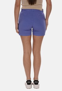 Pantaloni shorts viola con un design aderente, lunghezza a metà coscia e due tasche posteriori. Il materiale è liscio con una leggera brillantezza e senza fantasia.