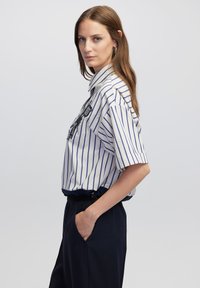 Camicia dal taglio comodo in bianco con righe blu navy, con colletto e maniche corte; abbinata a pantaloni blu navy.