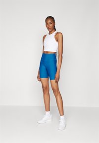 Shorts atletici blu a vita alta e top corto fitted bianco, entrambi realizzati in materiale elasticizzato. La modella indossa sneakers bianche e calzini alla caviglia.