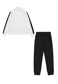 Witte zip-up jas met zwarte zijstrepen, zachte textuur en hoge kraag; gecombineerd met zwarte sweatpants met een elastische tailleband.