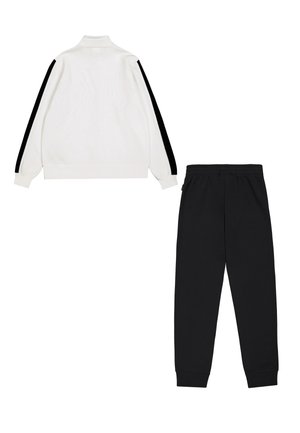 Giacca bianca con zip e strisce laterali nere, texture morbida e colletto alto; abbinata a pantaloni della tuta neri con vita elasticizzata.