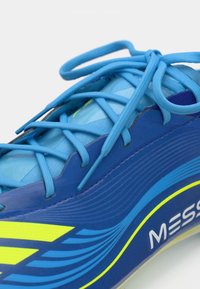 Blue athletic shoe with a textured surface, featuring yellow accents, bold lines, and a lacing system. Includes branding detail on the side.