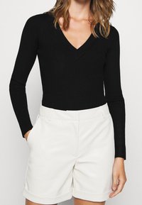 Zwarte geribbelde longsleeve met een diepe V-hals, gecombineerd met witte high-waisted shorts met zijzakken en opgerolde mouwen.