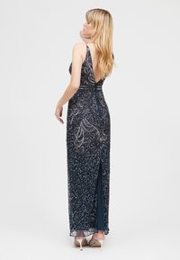 Lungo vestito blu navy con profondo scollo a V sul retro, ornato con perline argentate in un motivo a spirale, con uno spacco alto fino alla coscia e spalline delicate.