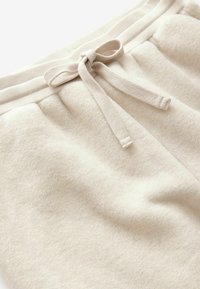 Vaaleanbeige fleece-housut, joissa on ribattu vyötärö ja nyöri. Pehmeä rakenne, jossa on sileä pinta ja hienovarainen kiilto.